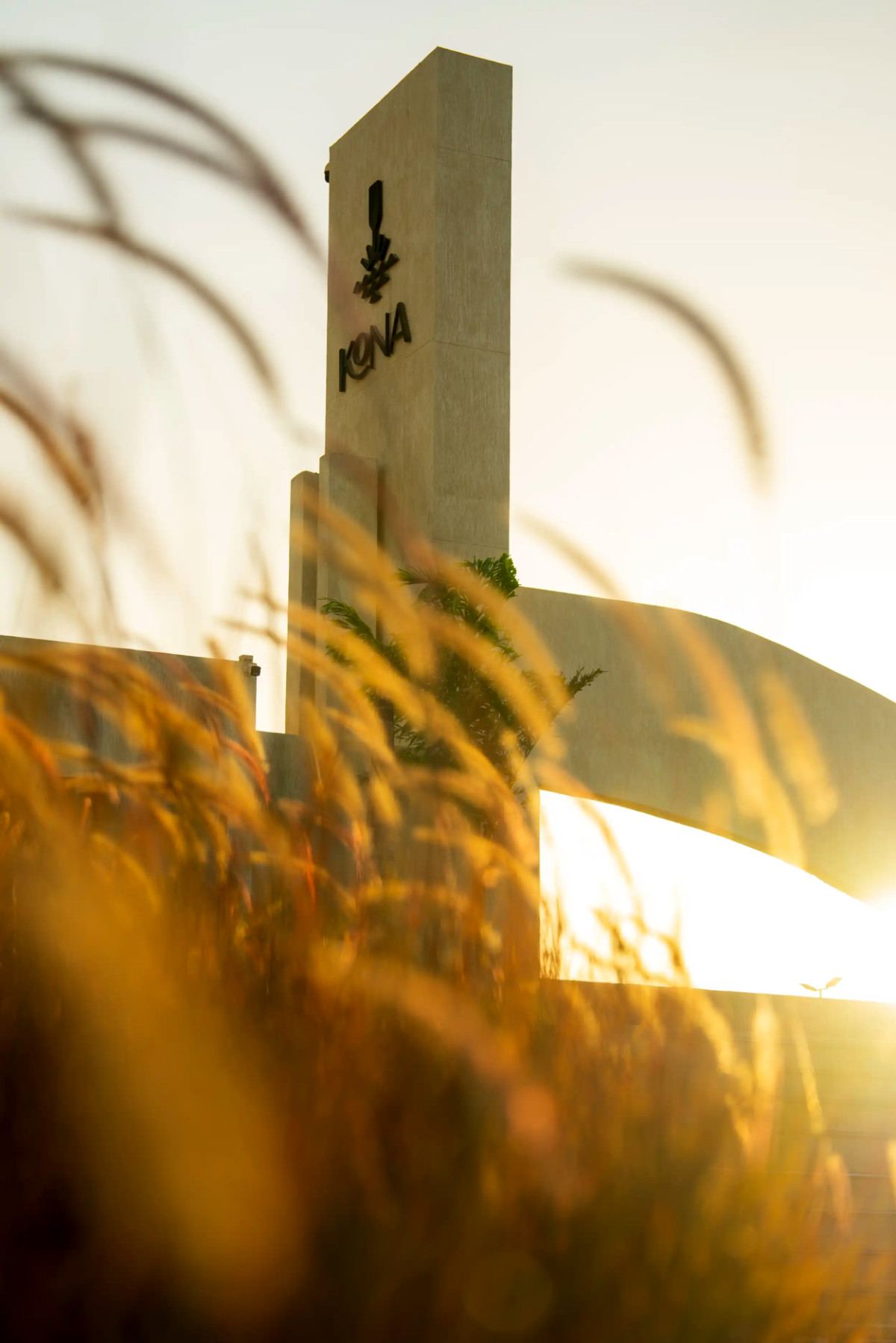 Kona Marine Sport Club’s entrance tower and logo glowing at sunset behind tall grasses