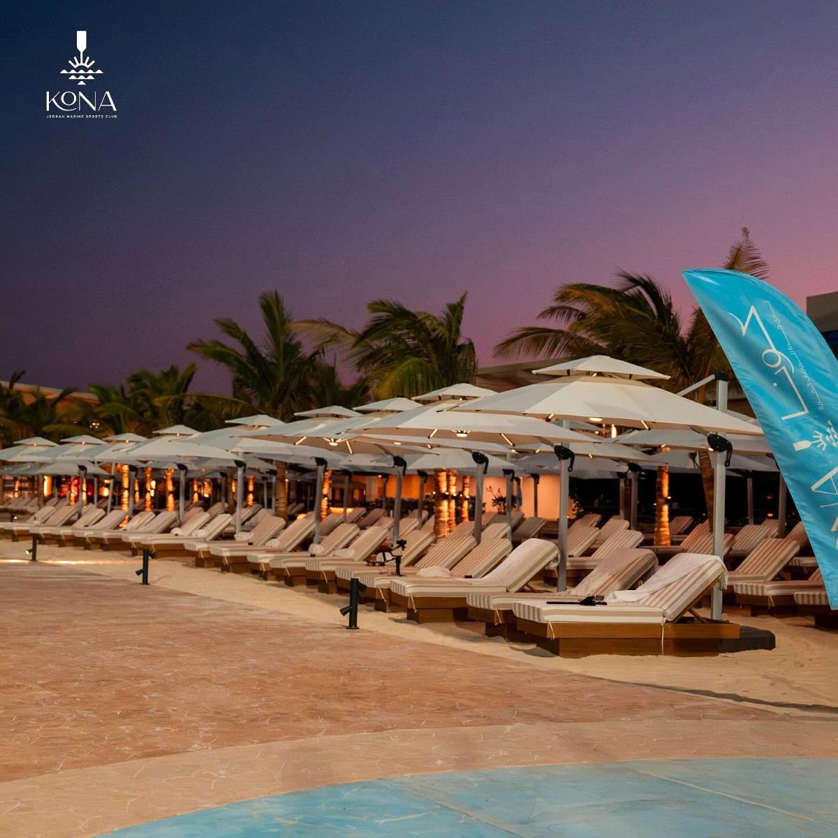 Rows of striped loungers under lit parasols at dusk at Kona Marine Sport Club