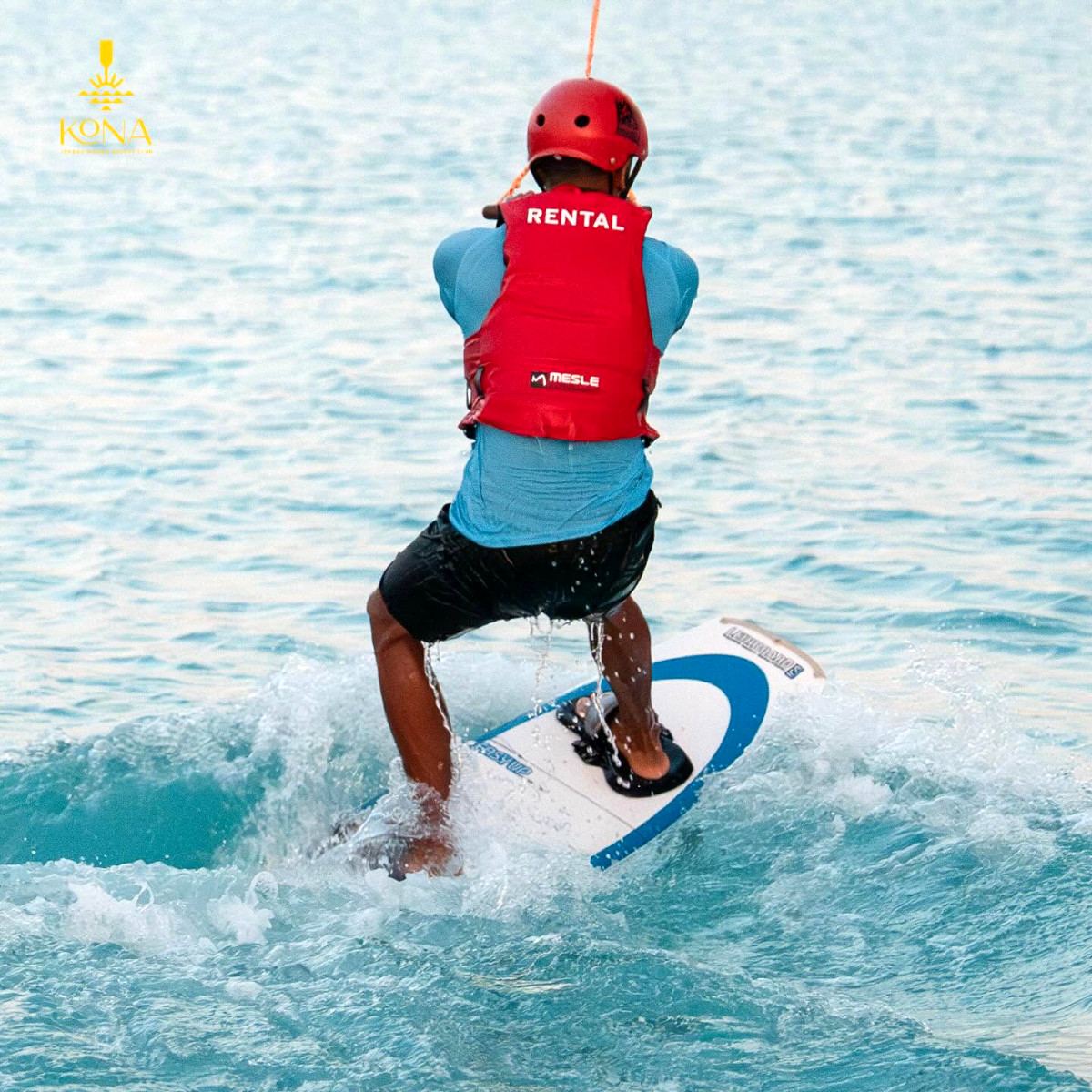 Wakeboarder in a red helmet and life vest carving through turquoise water at Kona Marine Sport Club