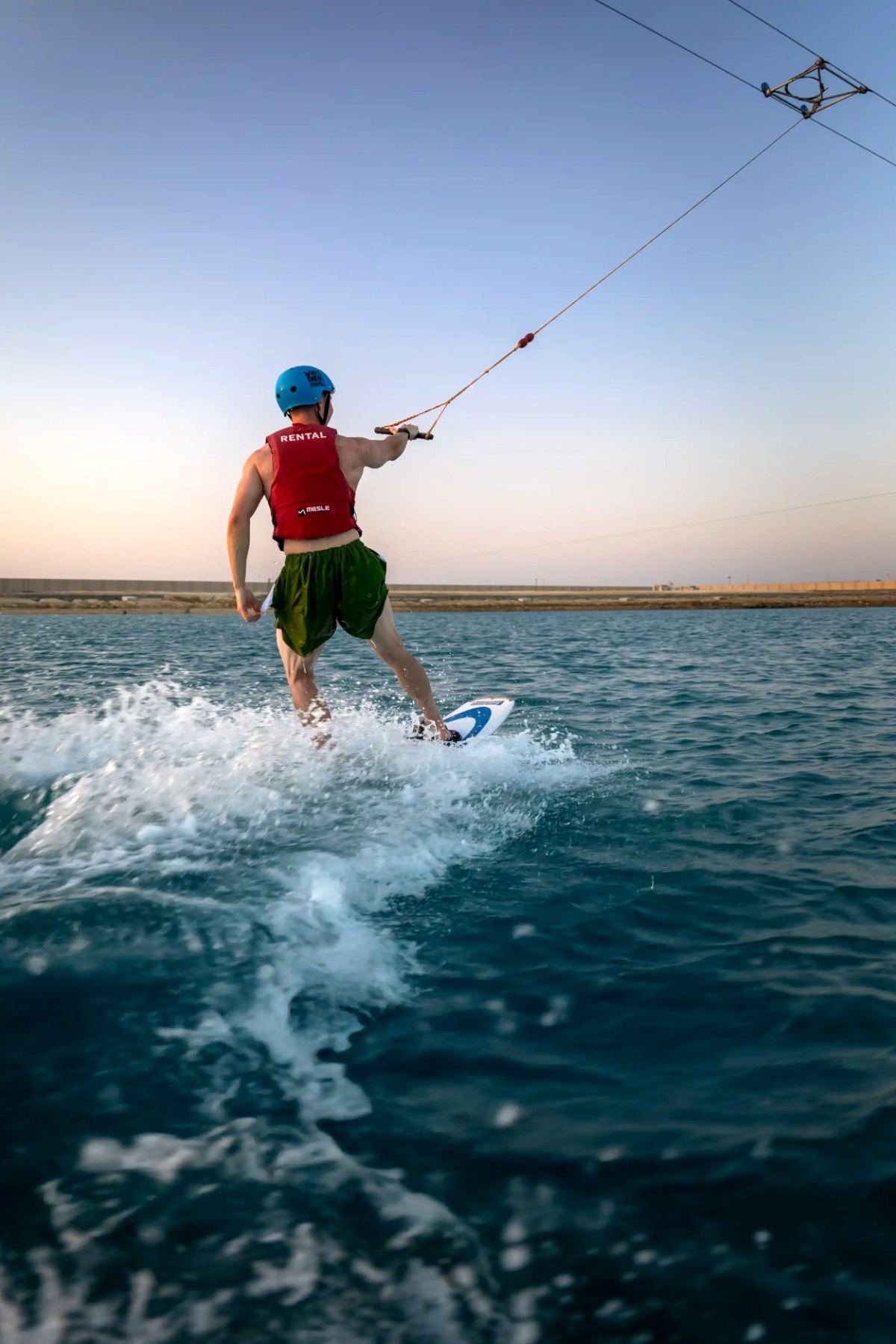 Cable wakeboarder in a helmet and life vest carving across the lagoon at Kona Marine Sport Club