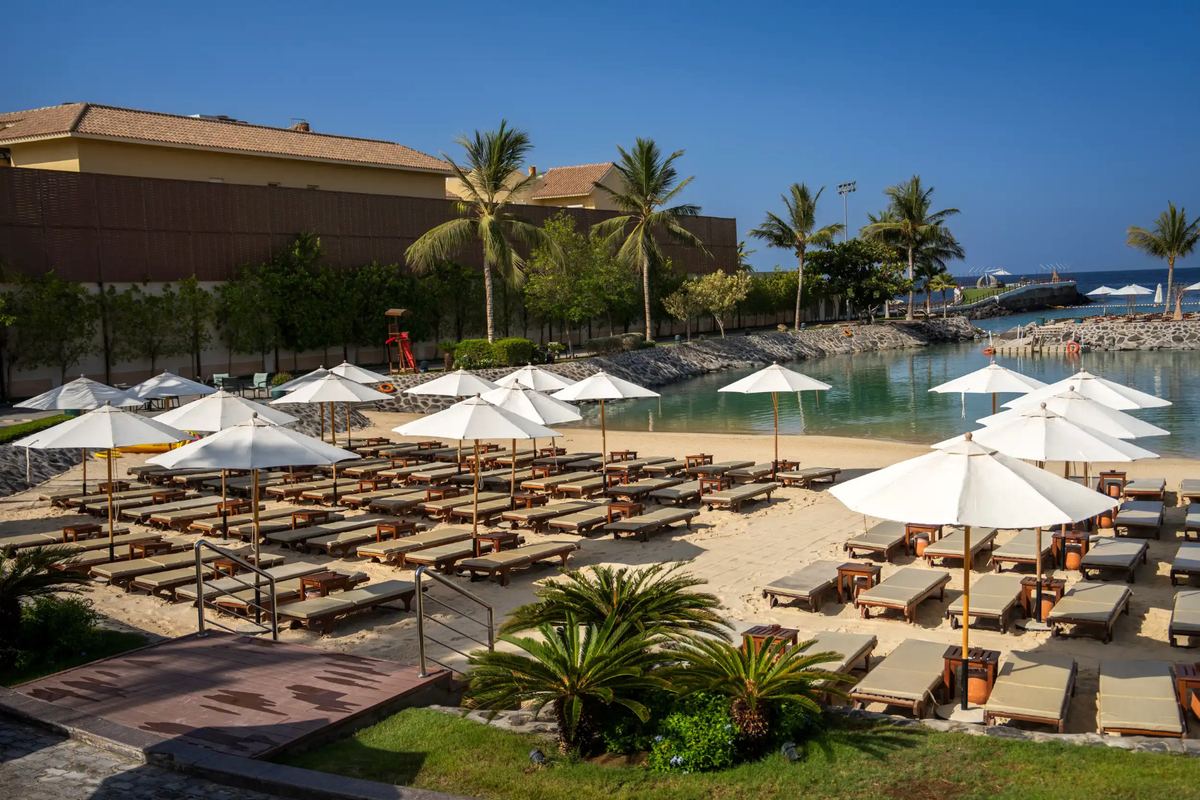 Rows of cushioned loungers and white parasols on La Maison D’Obhur’s sandy lagoon beach