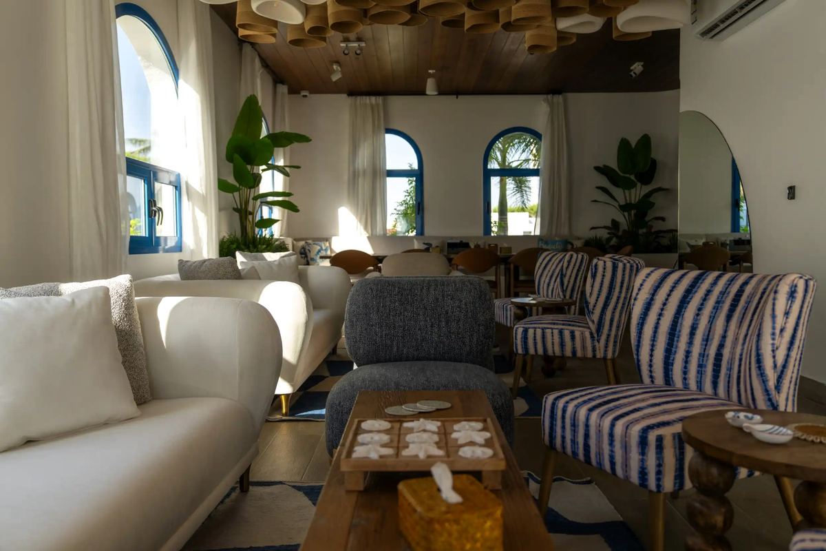 Bright lounge with arched blue windows, white sofas and striped armchairs at Le Pont de l’Amitié
