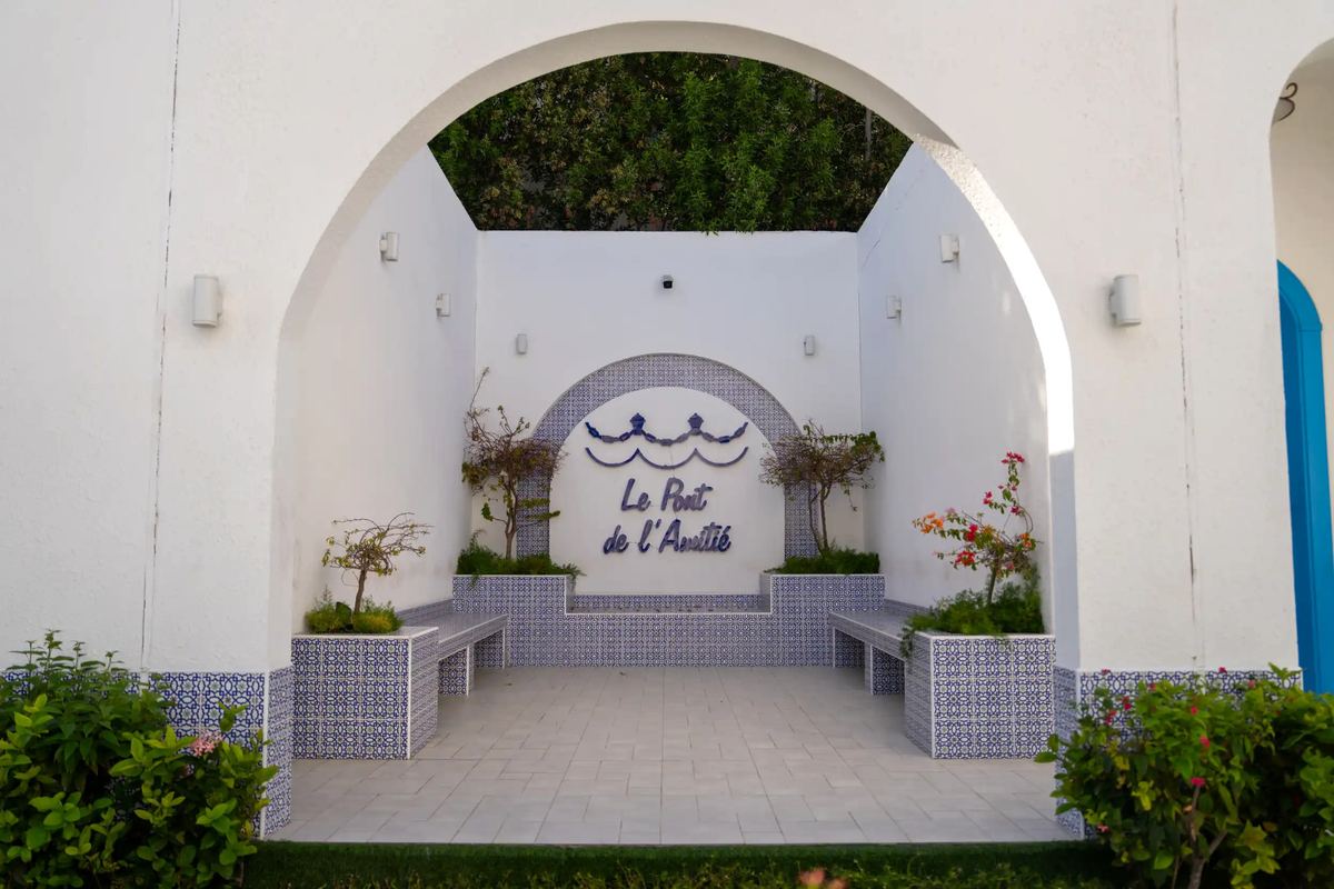 Whitewashed archway framing a blue-tiled courtyard with Le Pont de l’Amitié signage
