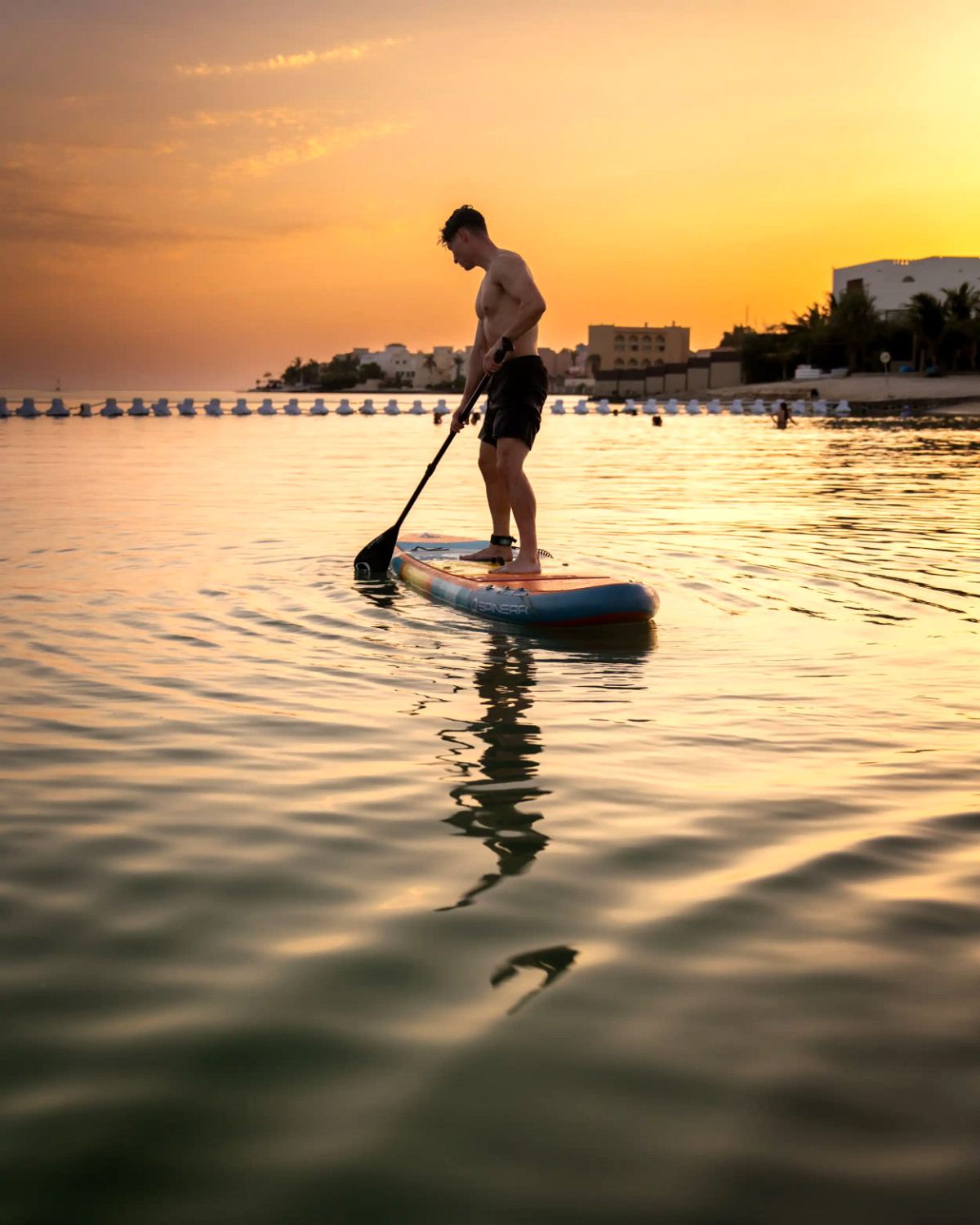 Paddleboarder gliding across calm water at sunset at Shades Beach Club
