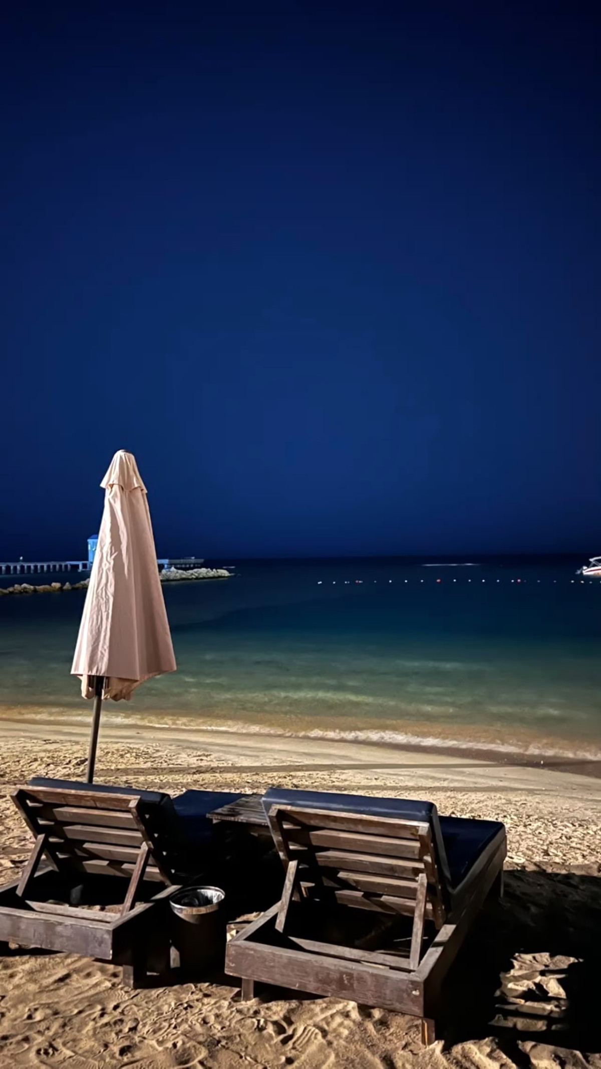 Two wooden sun loungers and a folded parasol facing the sea at night at Siyal Resort